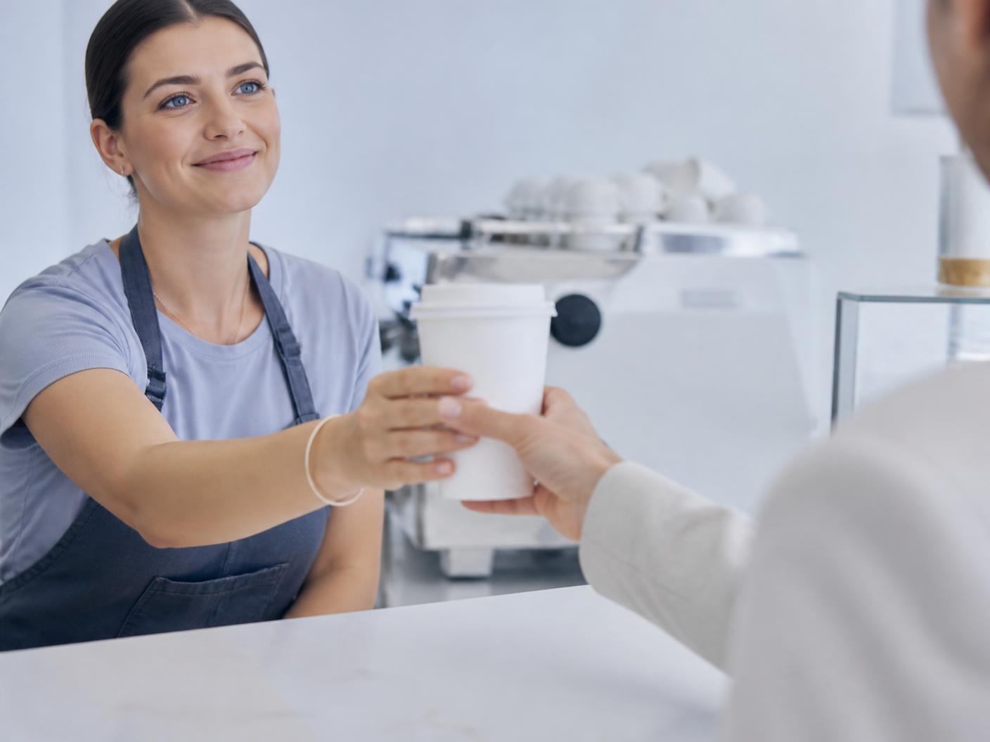 A barista handing coffee to a returning customer
